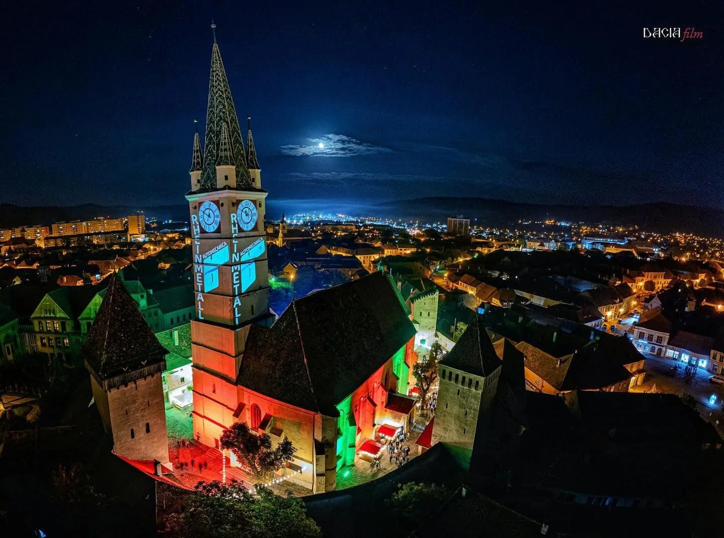 Turnul unei biserici iluminat în mai multe culori, noaptea
