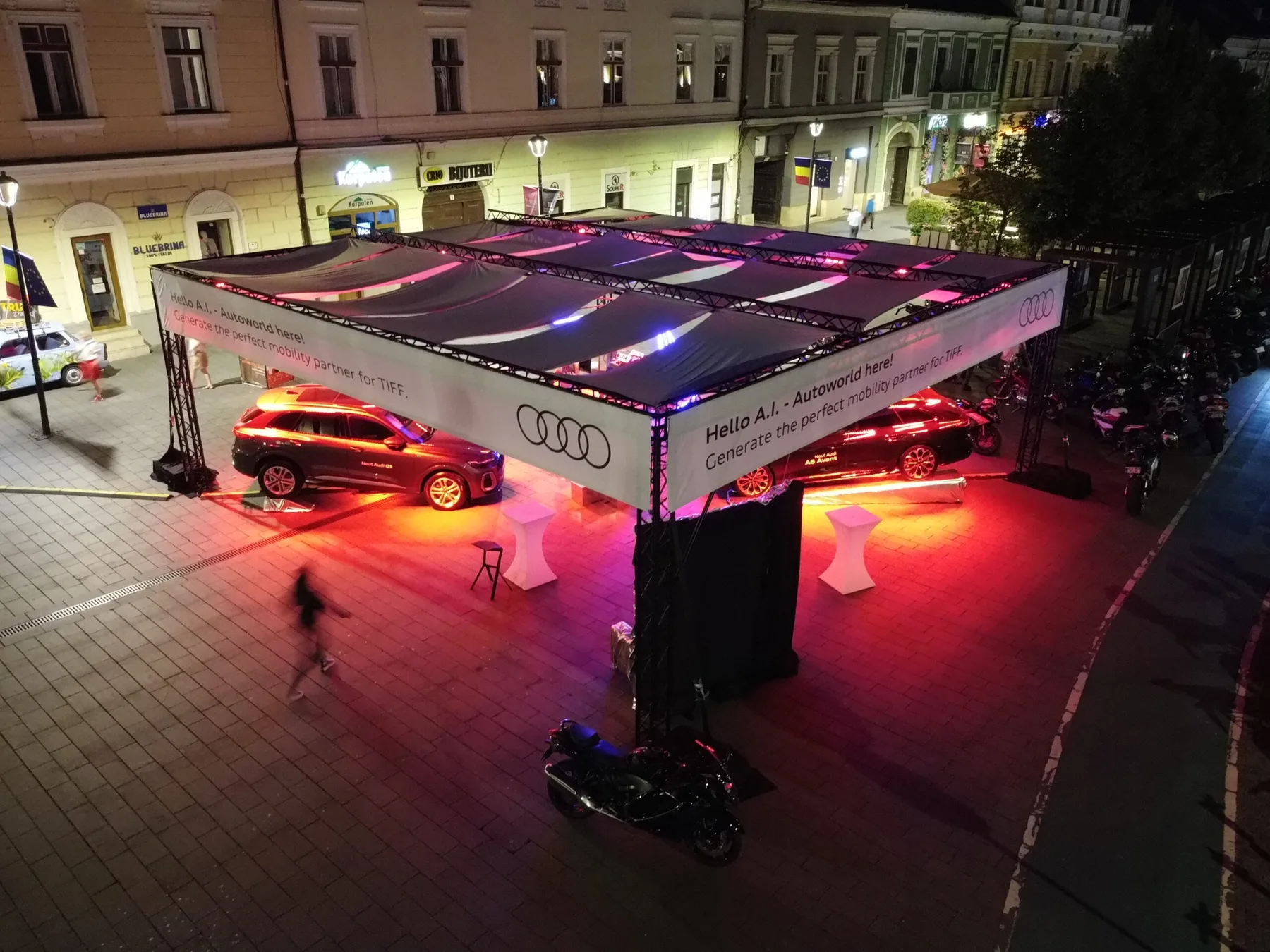 Copertină truss dreptunghiulară peste o expoziție auto, iluminată roșu într-o piață